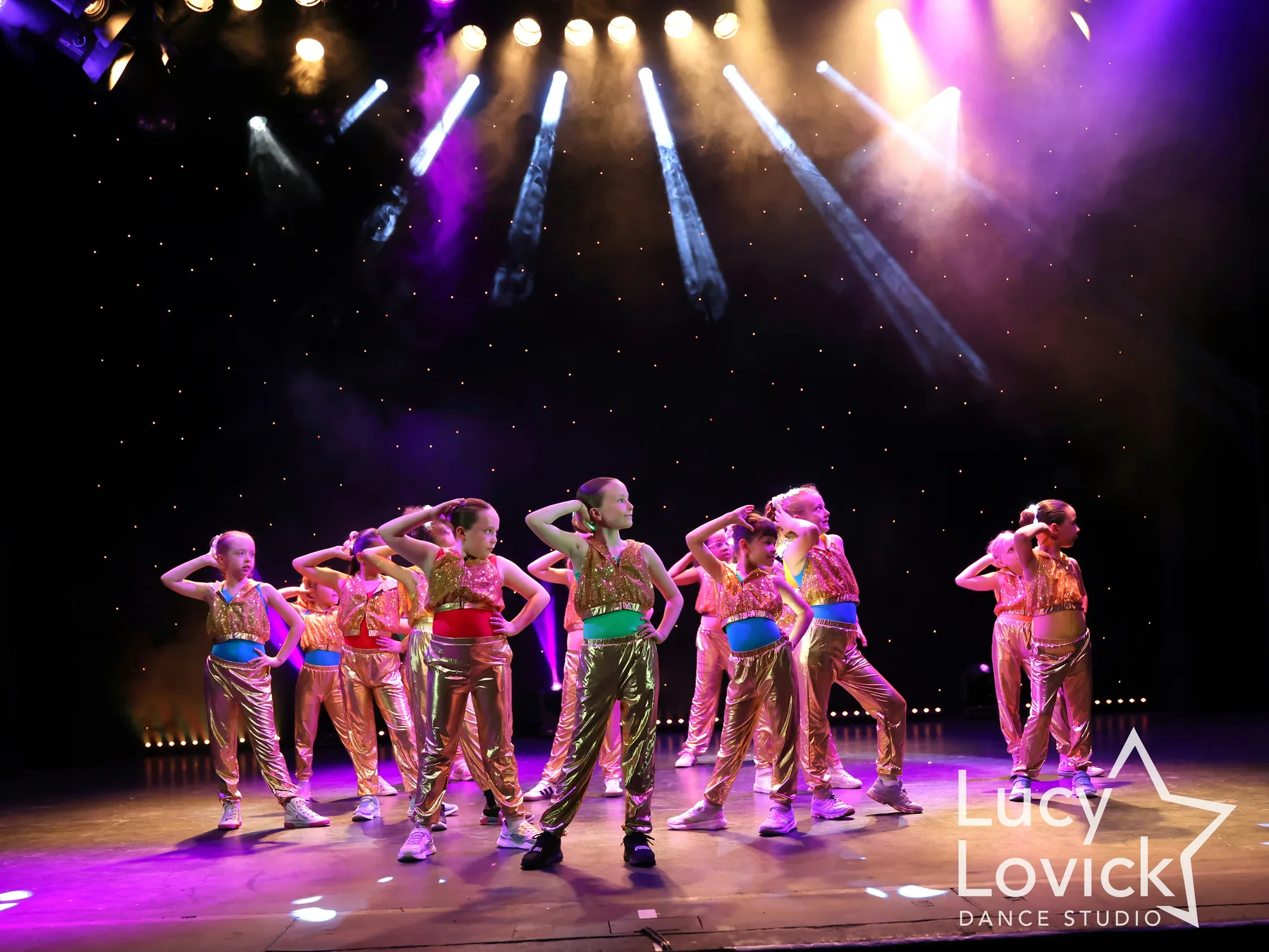 LLDS dancers in gold costumes posing on stage under theatre lights